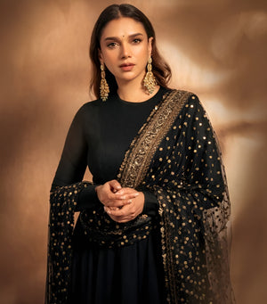 Woman wearing a black outfit with gold embroidery against a warm brown background