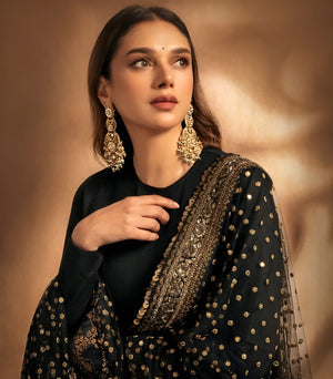 Woman wearing a black and gold traditional outfit with jewelry against a warm-toned background