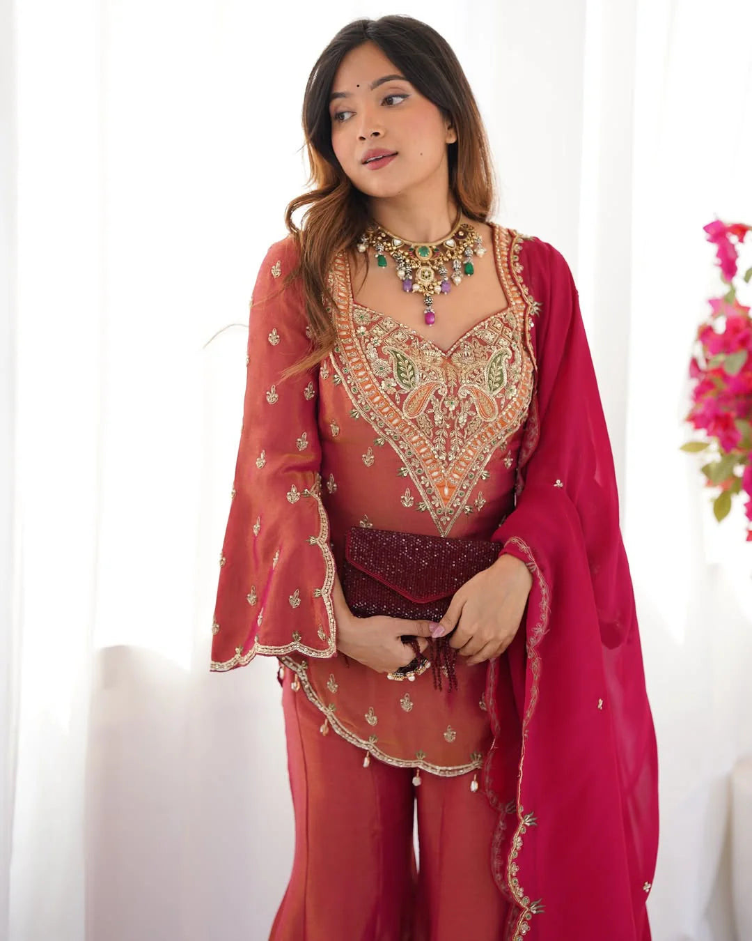 Woman wearing a traditional embroidered outfit with a pink dupatta against a white background