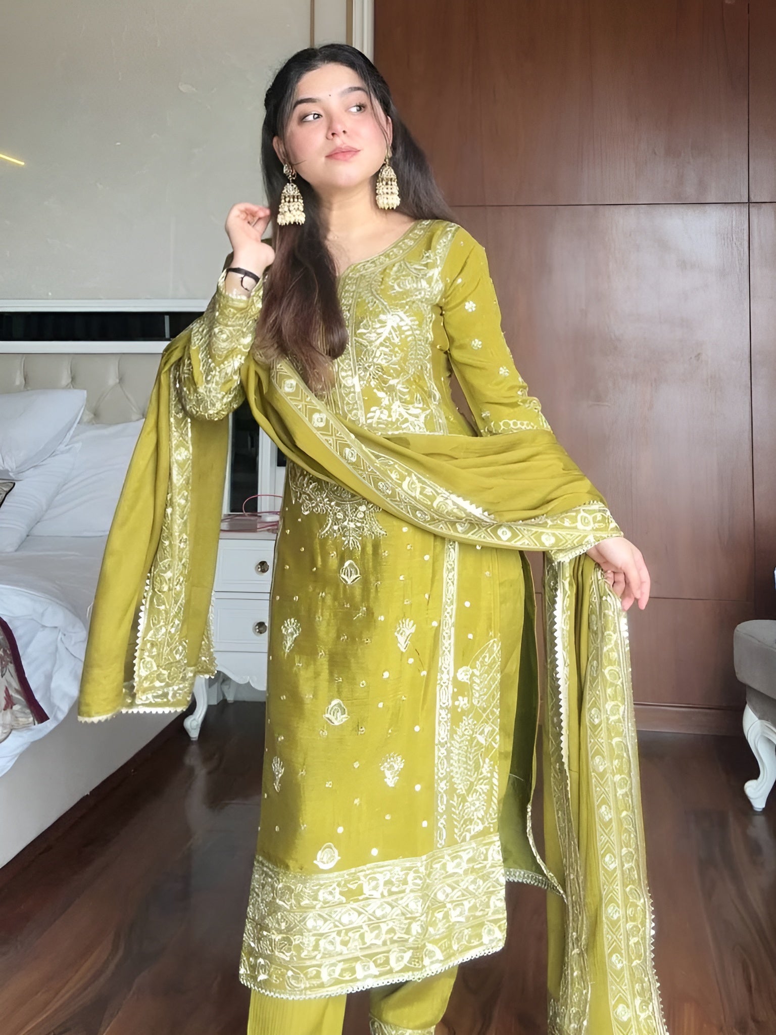 Woman wearing a green embroidered traditional outfit in a room.