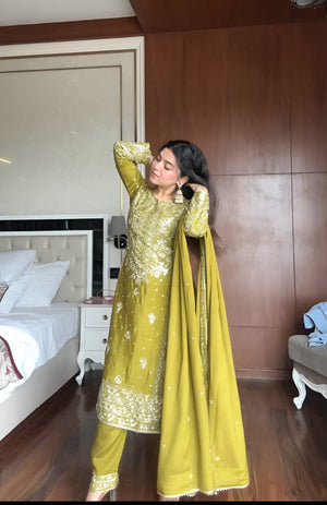 Woman in a green traditional outfit standing in a bedroom.