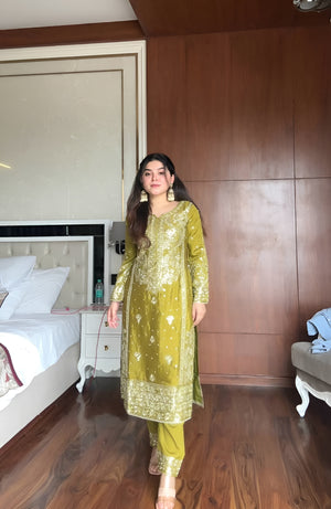 Woman in a green traditional outfit standing in a bedroom.