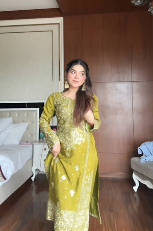 Woman in a green traditional outfit standing in a bedroom.