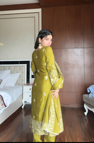 Woman in a green traditional outfit standing in a bedroom.