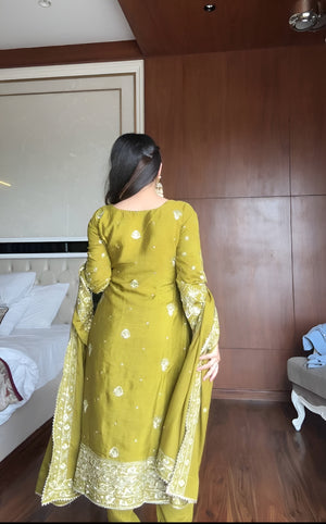 Woman in a green traditional outfit standing in a room with wooden paneling.