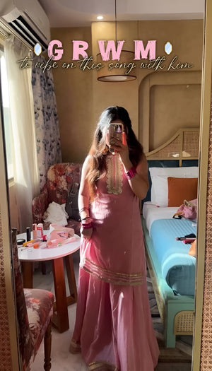 Person wearing a pink traditional Diya Organza Sharara Set with Sequin_Mirror Work outfit in a room with a bed and sofa.Lahariya.com