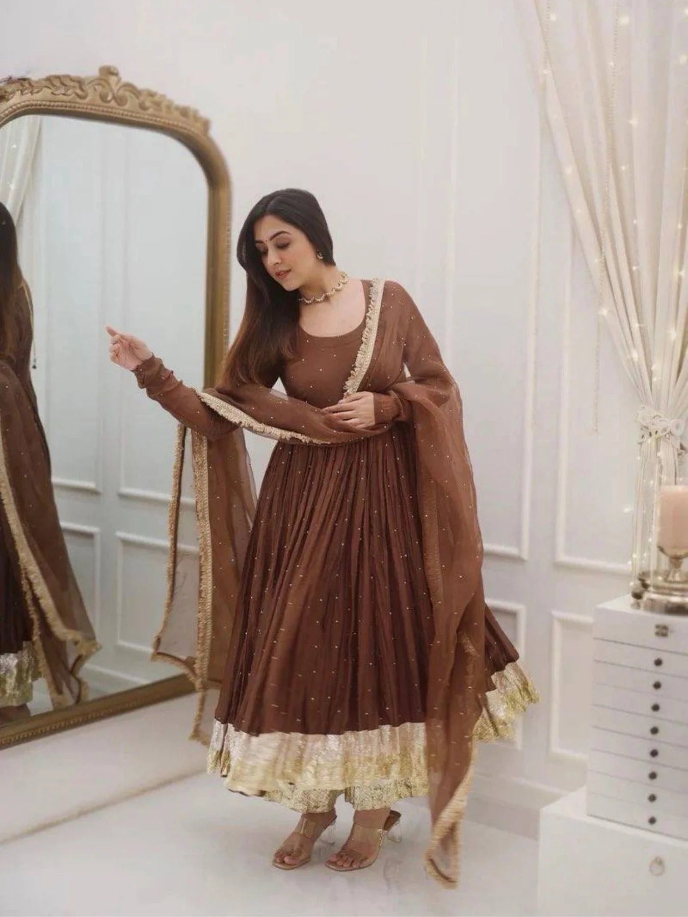 Woman in a brown and gold traditional outfit standing in front of a mirror.