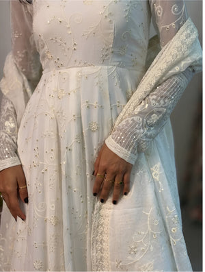 Close-up of a person wearing a white embroidered dress with intricate patterns.