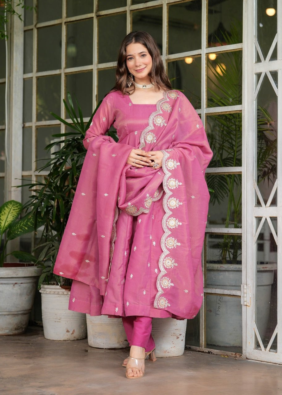 Woman in a pink traditional outfit Riya Pink Georgette Kurti Pant Set with Embroidered Dupatta standing in front of a glass door with plants.