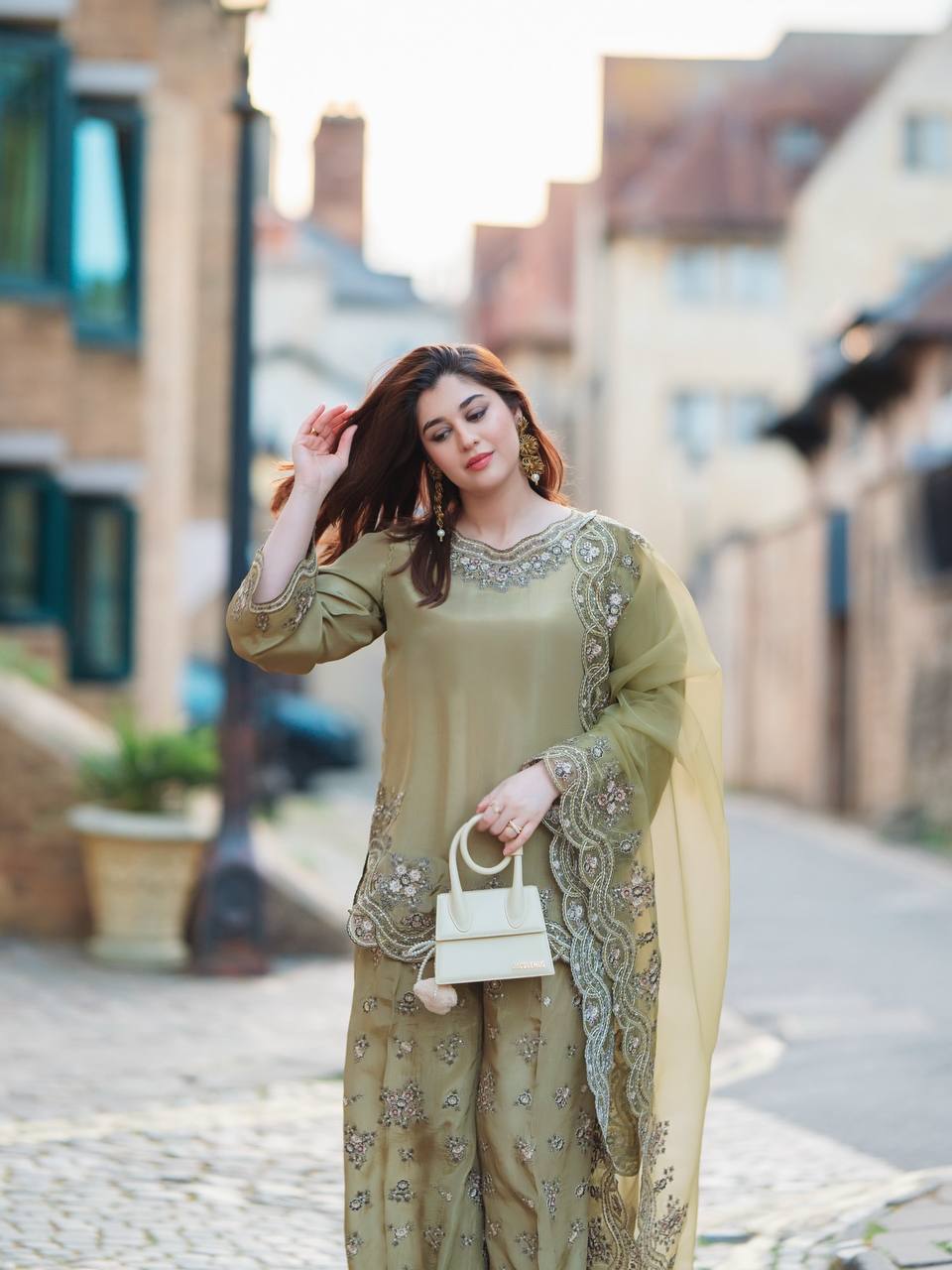 Woman in a green traditional outfit with embroidery walking on a street.