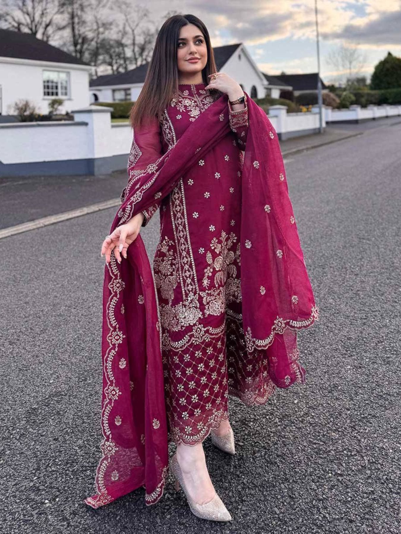 Woman in a red embroidered outfit with a matching dupatta standing on a road.
