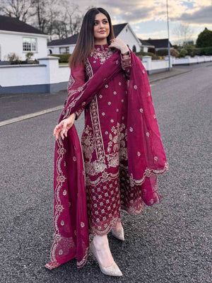 Woman in a red embroidered outfit with a matching dupatta standing on a road.