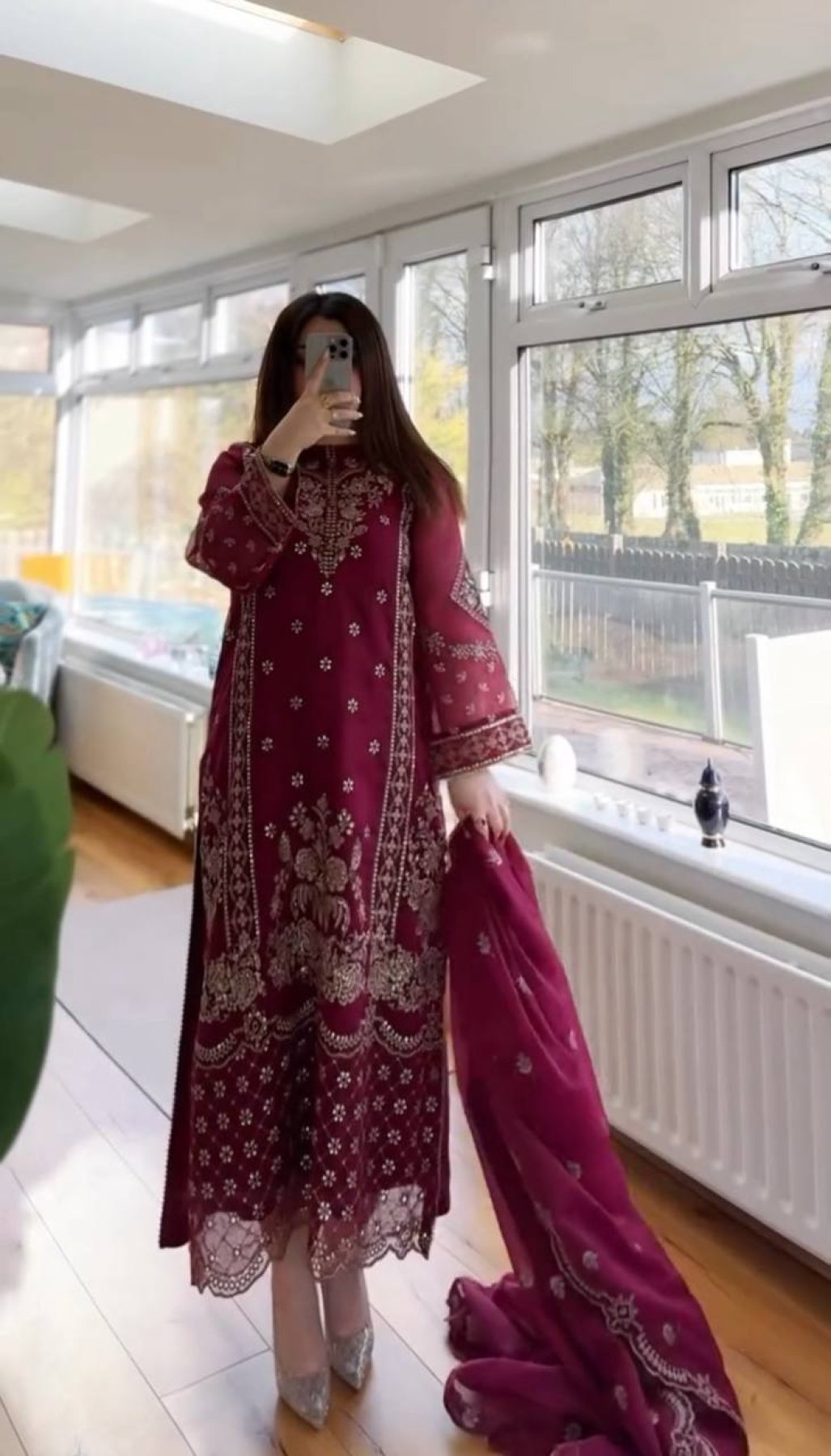 Person wearing a wine embroidered outfit in a room with large windows.