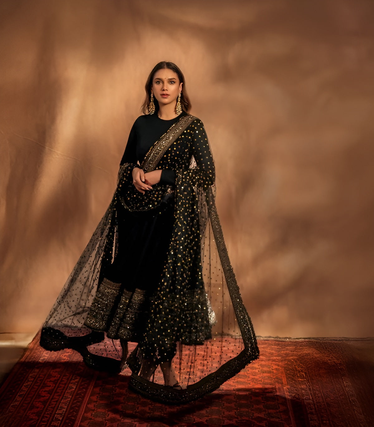 Woman wearing a black and gold traditional outfit with a draped fabric against a warm-toned background.