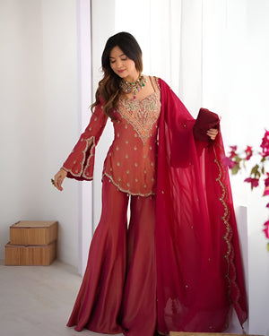 Woman in a red traditional outfit with embroidery, holding a matching dupatta.