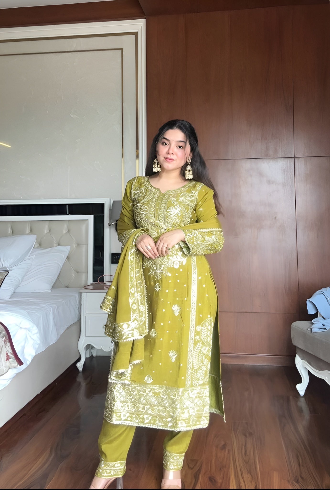Woman in a green traditional outfit standing in a bedroom.