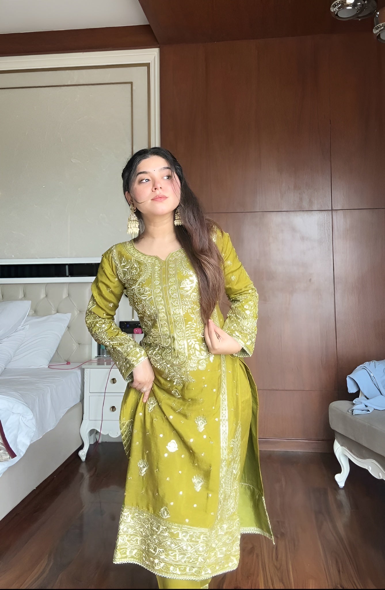 Woman in a green traditional outfit standing in a bedroom.