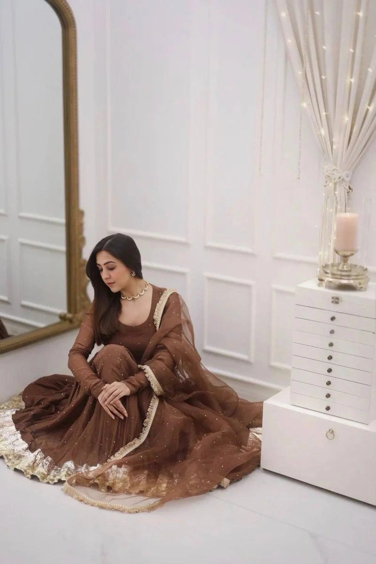 Woman in a brown dress sitting on the floor in a room with white walls and decor.
