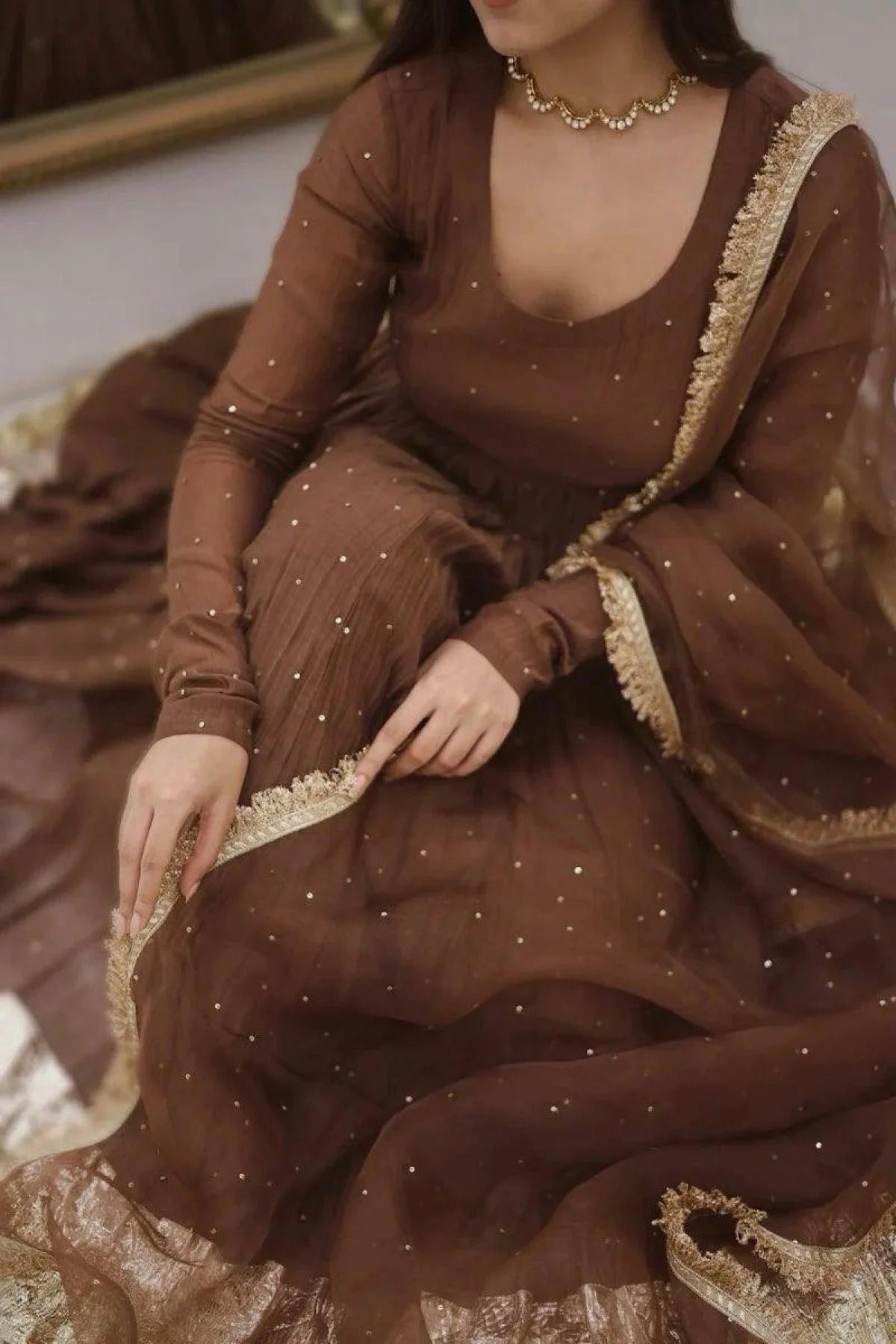 Woman wearing a brown dress with gold trim sitting on a couch.