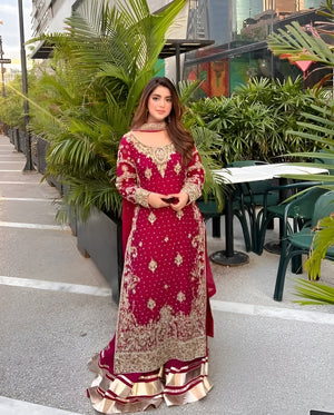 Woman in a red and gold traditional outfit standing outdoors with greenery in the background