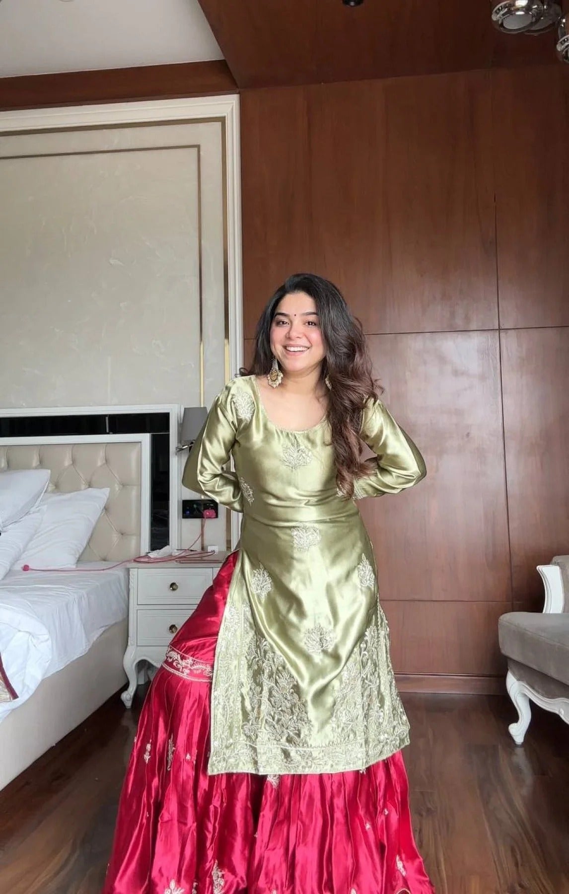 Woman in a green and red traditional outfit standing in a bedroom.