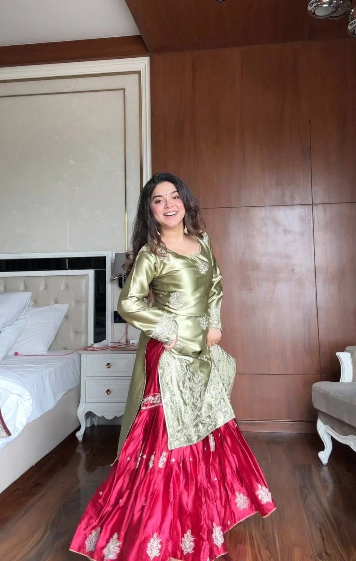 Woman in a green and pink traditional outfit standing in a bedroom.