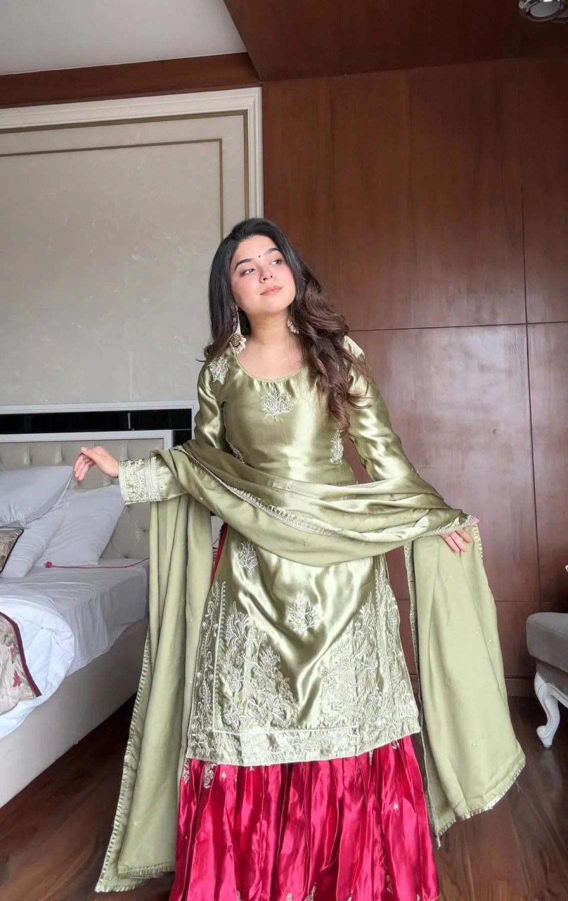 Woman in a green and red traditional outfit standing in a room with wooden paneling.