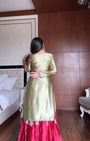 Woman in a green and red traditional outfit standing in a room with wooden paneling.