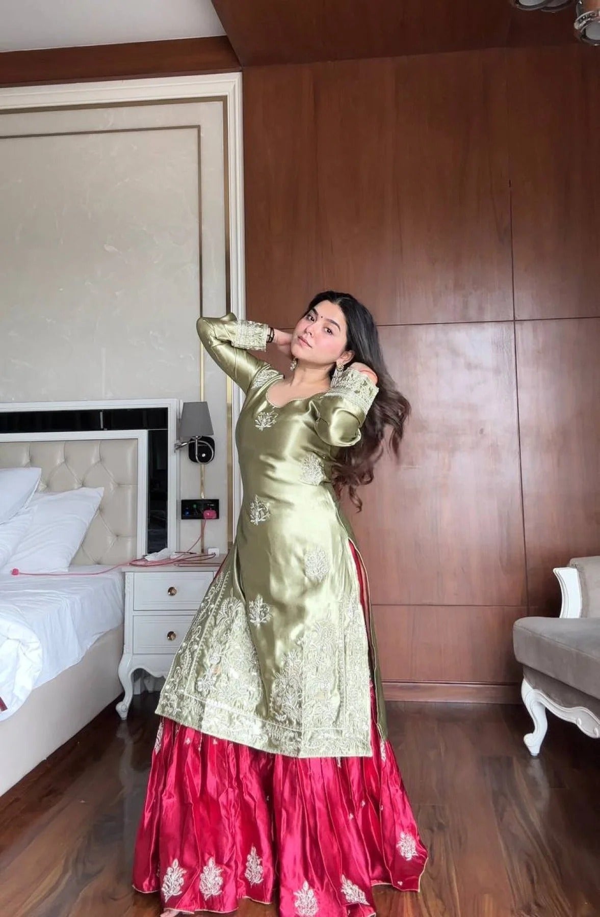 Woman in a gold and pink traditional outfit standing in a bedroom.