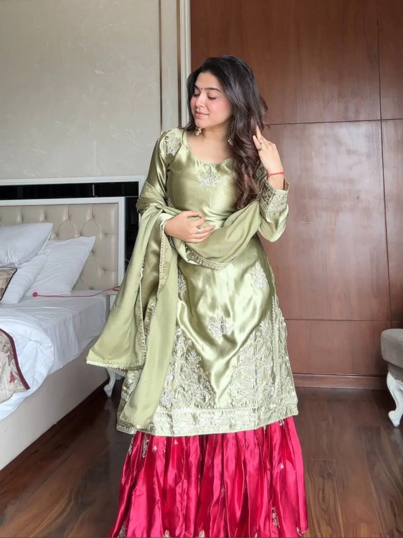 Woman in a green and pink traditional outfit standing in a bedroom.
