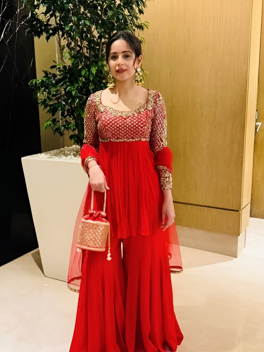 Woman in a red traditional outfit holding a handbag indoors.