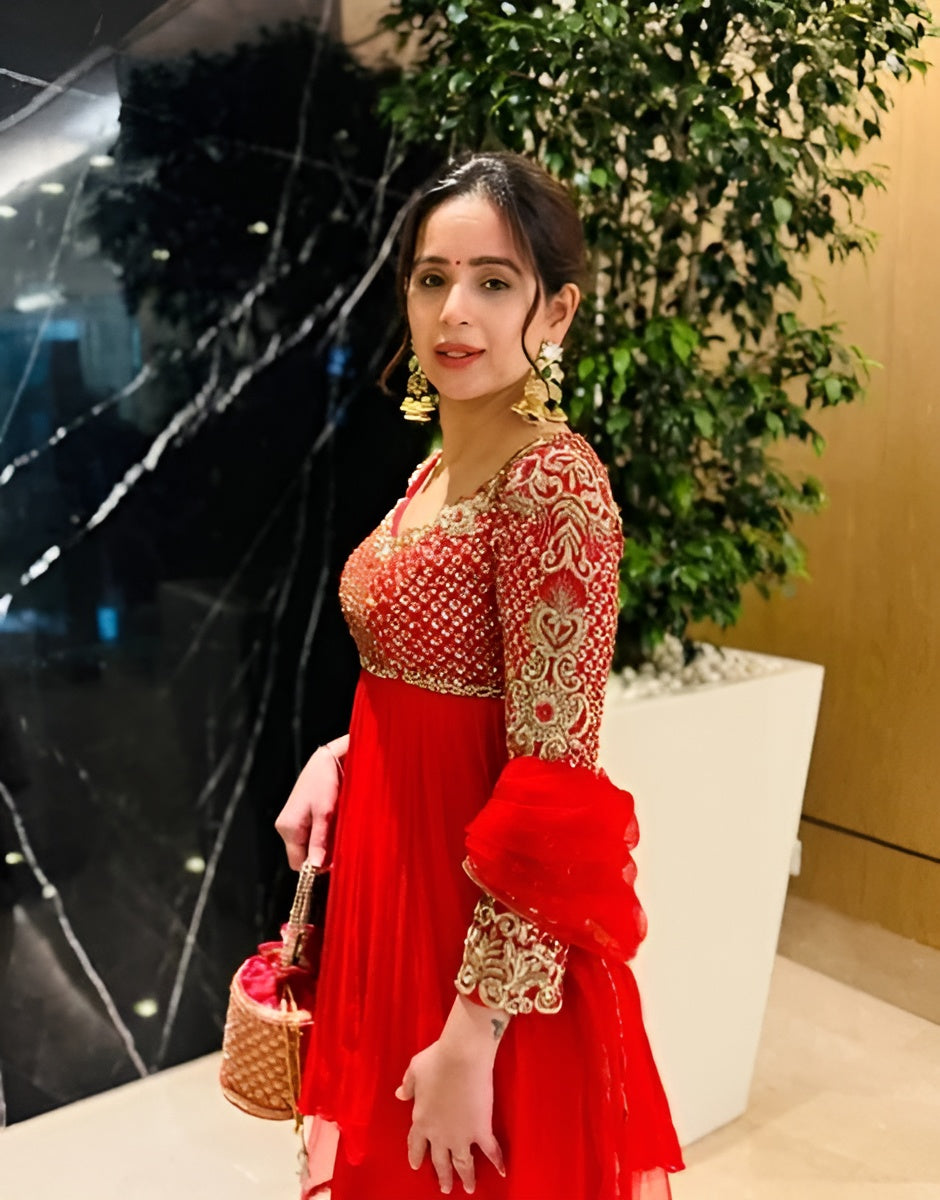 Woman in a red and gold traditional outfit holding a small bag indoors.
