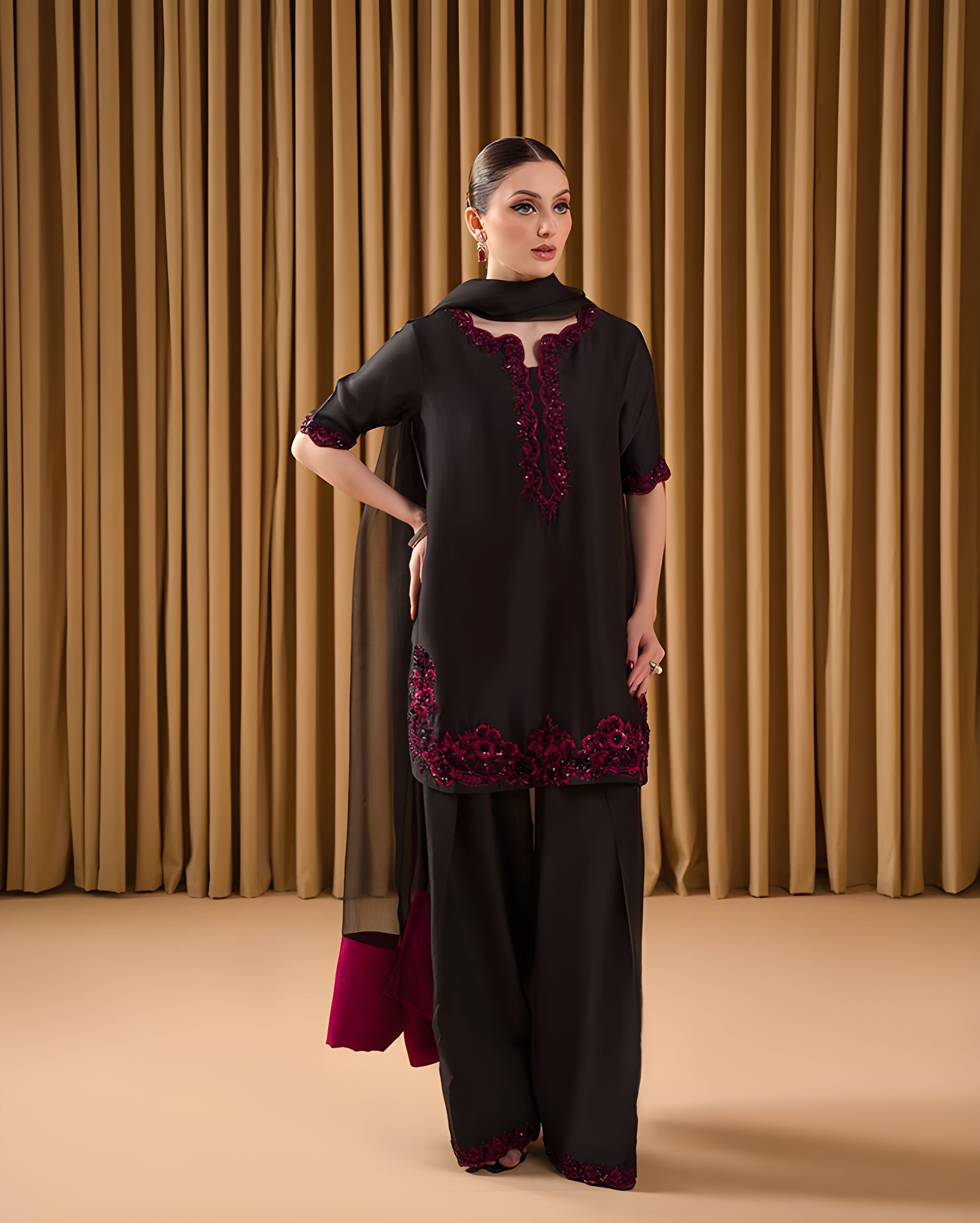 Woman wearing a black and red traditional outfit against a brown curtain background