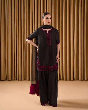 Woman wearing a black and red traditional outfit against a brown curtain background