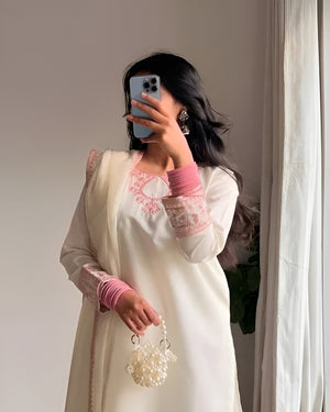 Woman taking a mirror selfie wearing a white outfit with pink accents and holding a pearl-handled bag.