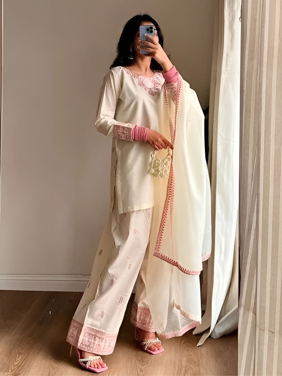 Woman wearing a traditional outfit with a white and pink dupatta in a room.
