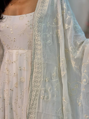 white embroidered dupatta draped over a white outfit with gold detailing.
