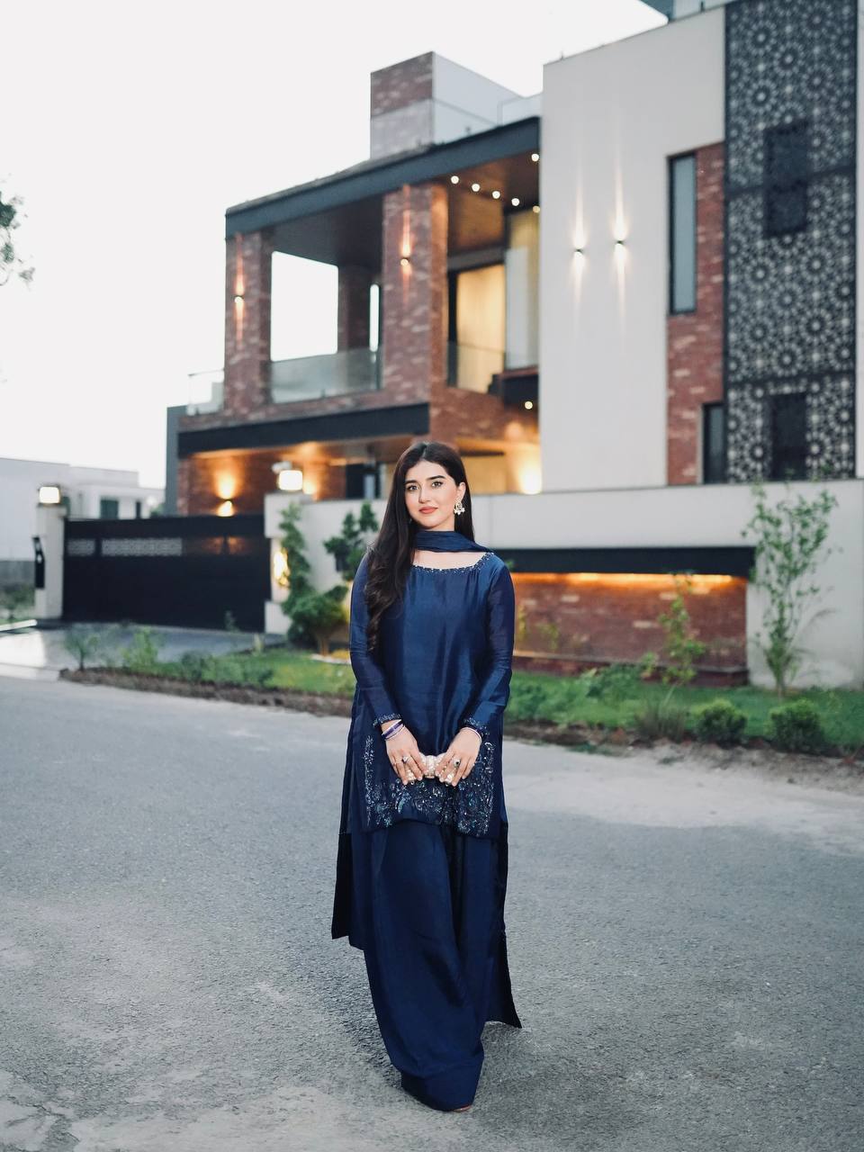 Woman in a blue traditional outfit standing on a street with trees in the background
