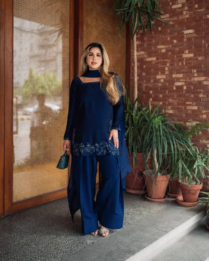 Woman in a blue traditional outfit standing on a street with trees in the background