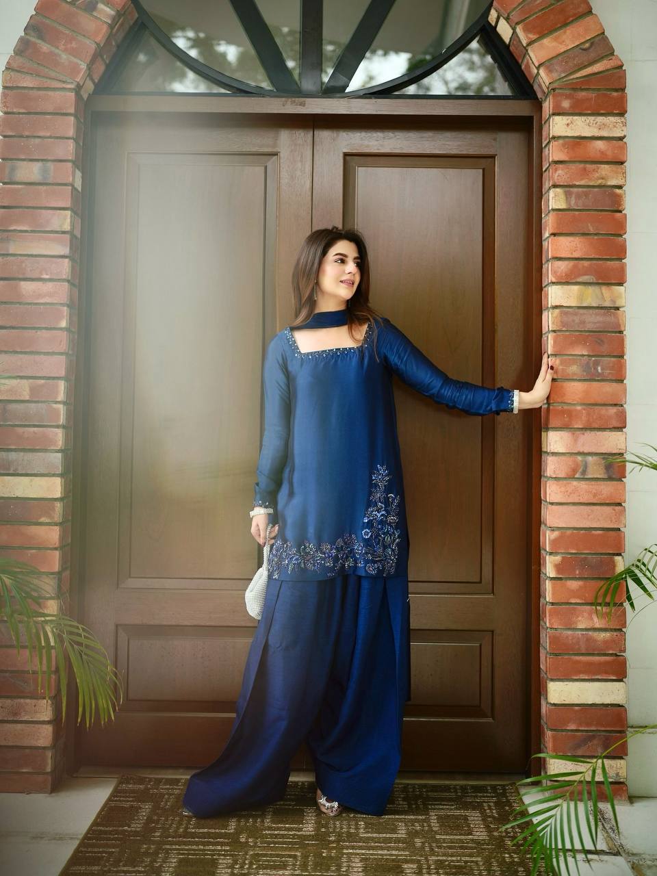 Woman in a blue traditional outfit standing on a street with trees in the background