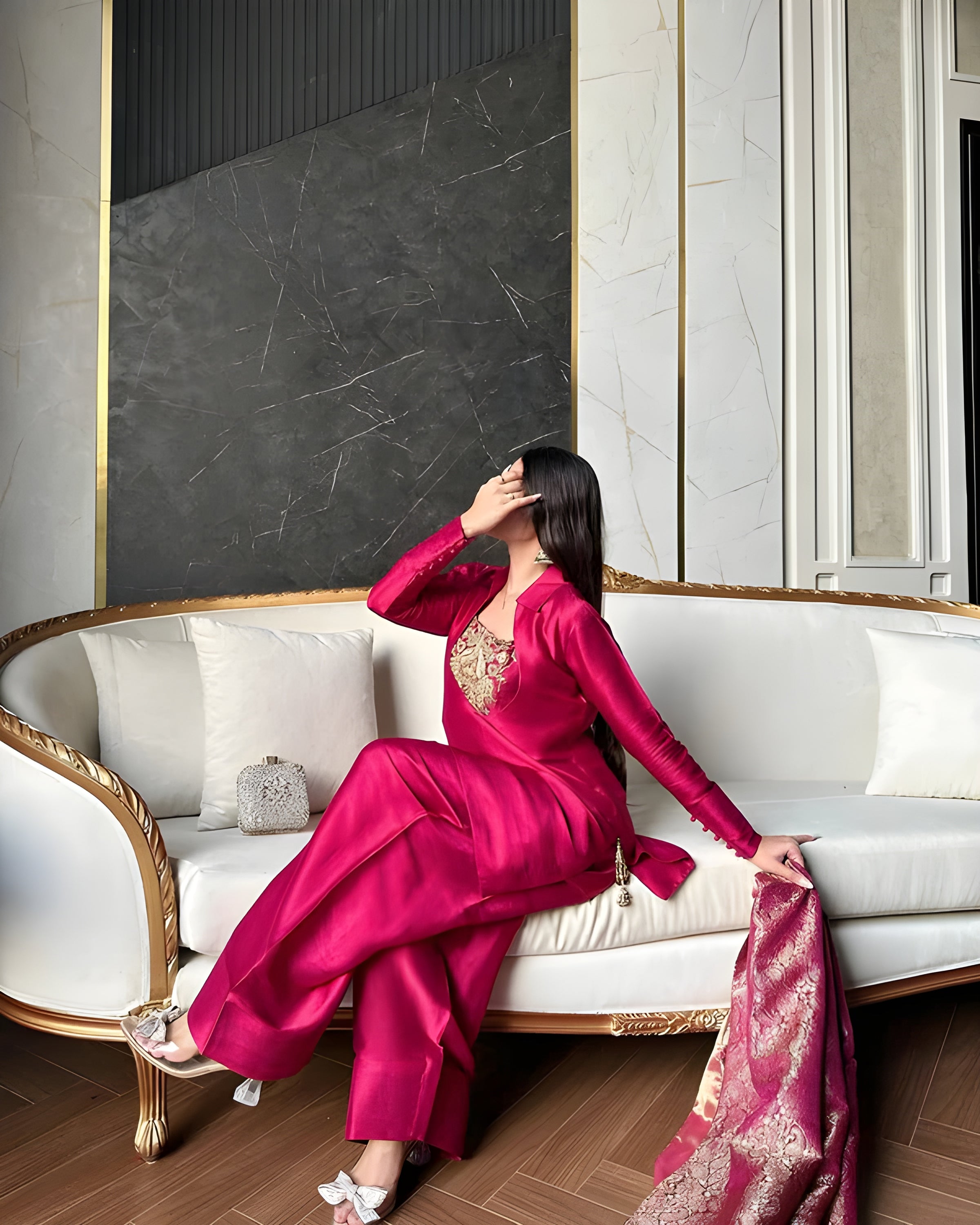 Woman in a vibrant pink outfit sitting on a white sofa in an elegant interior setting.