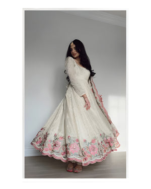 Woman wearing a white dress with floral embroidery in a minimal indoor setting
