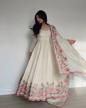 Woman wearing a white and pink embroidered traditional outfit against a plain background