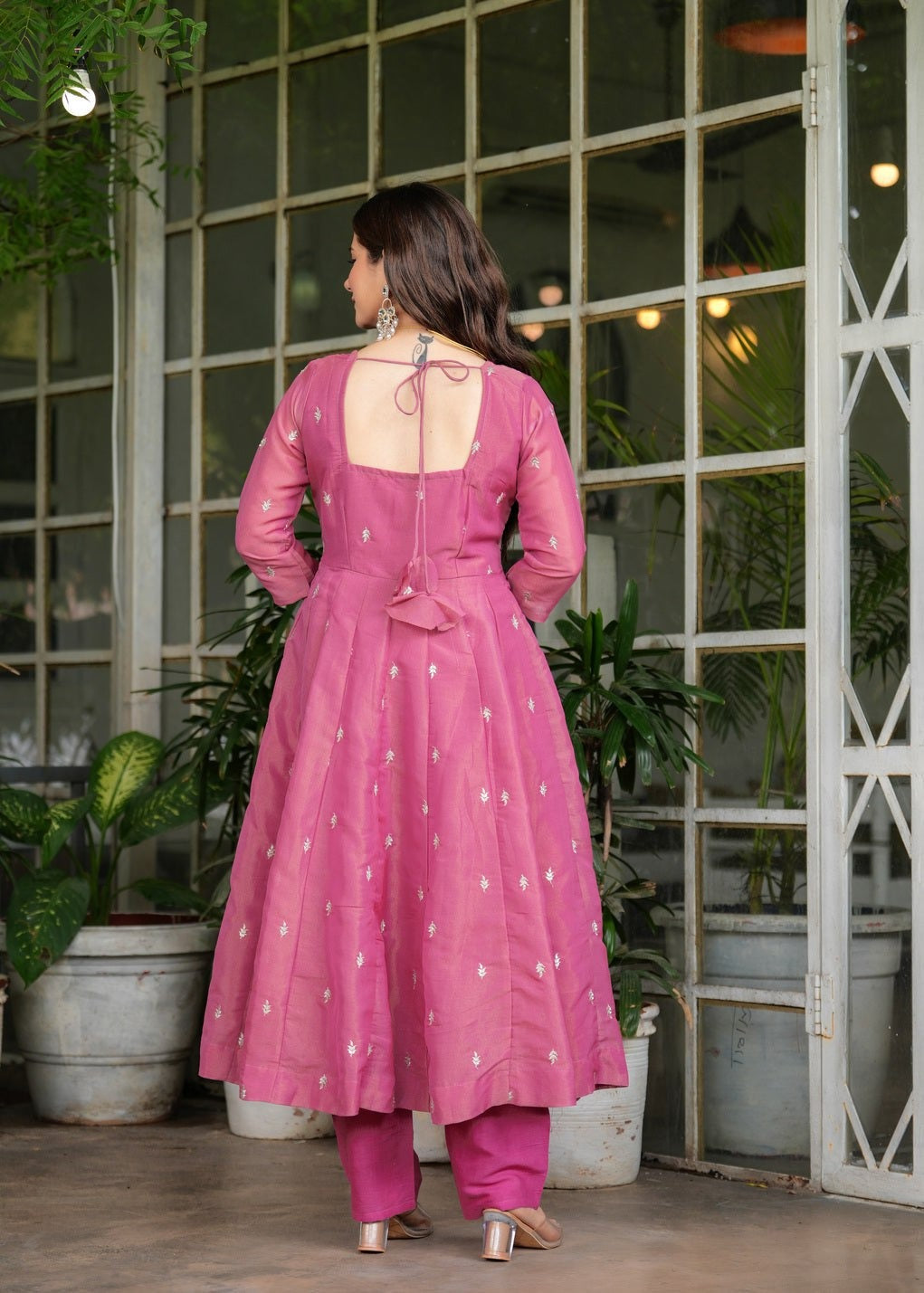 Woman in a pink traditional outfit Riya Pink Georgette Kurti Pant Set with Embroidered Dupatta standing in front of a glass door with plants.