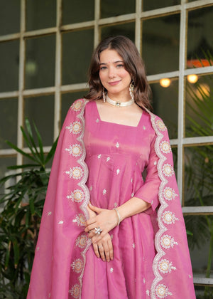 Woman in a pink traditional outfit Riya Pink Georgette Kurti Pant Set with Embroidered Dupatta standing in front of a glass door with plants.