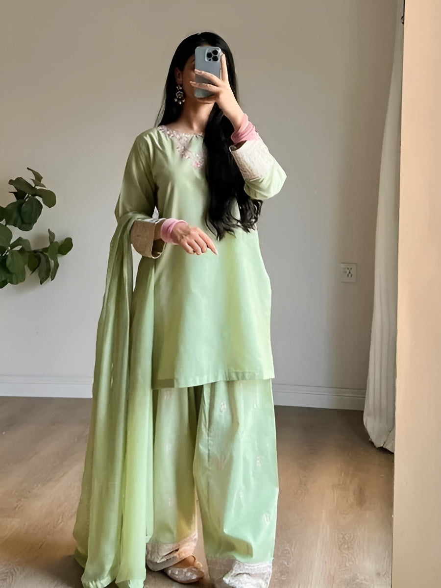 Person wearing a light green traditional outfit with a white lace top, standing indoors.