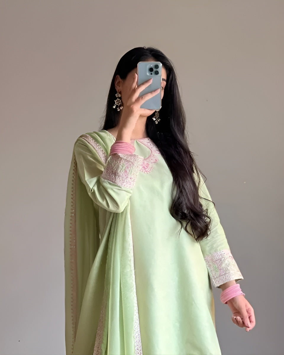 Person wearing a light green traditional outfit with pink accents, holding a phone.