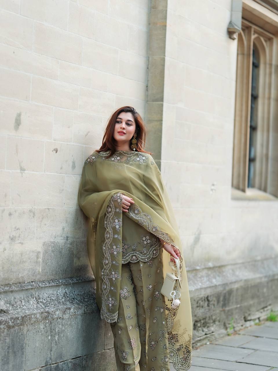 Woman in a green traditional outfit standing against a stone wall.