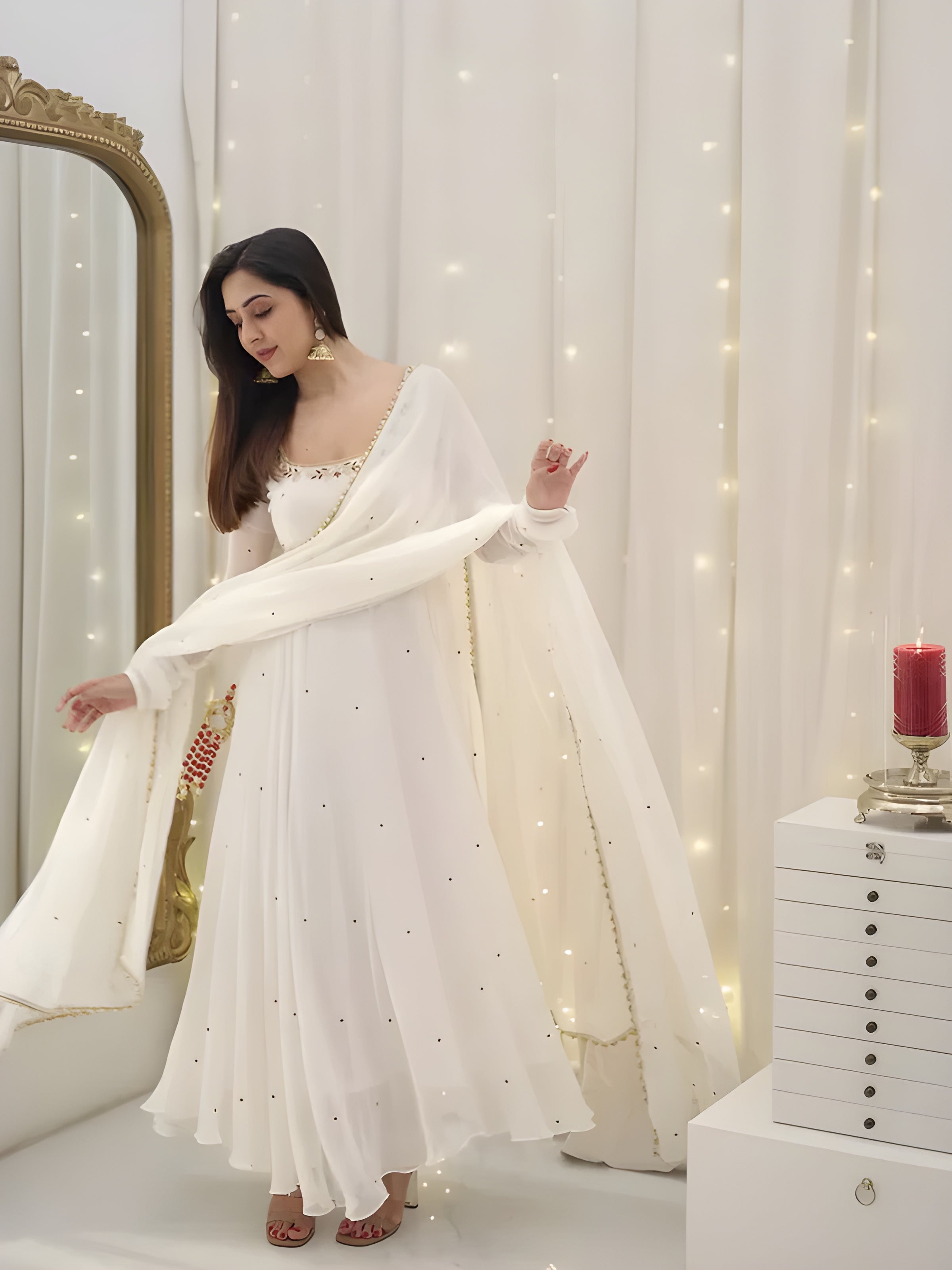 Woman in a white dress with a sheer dupatta in a decorated room with fairy lights.