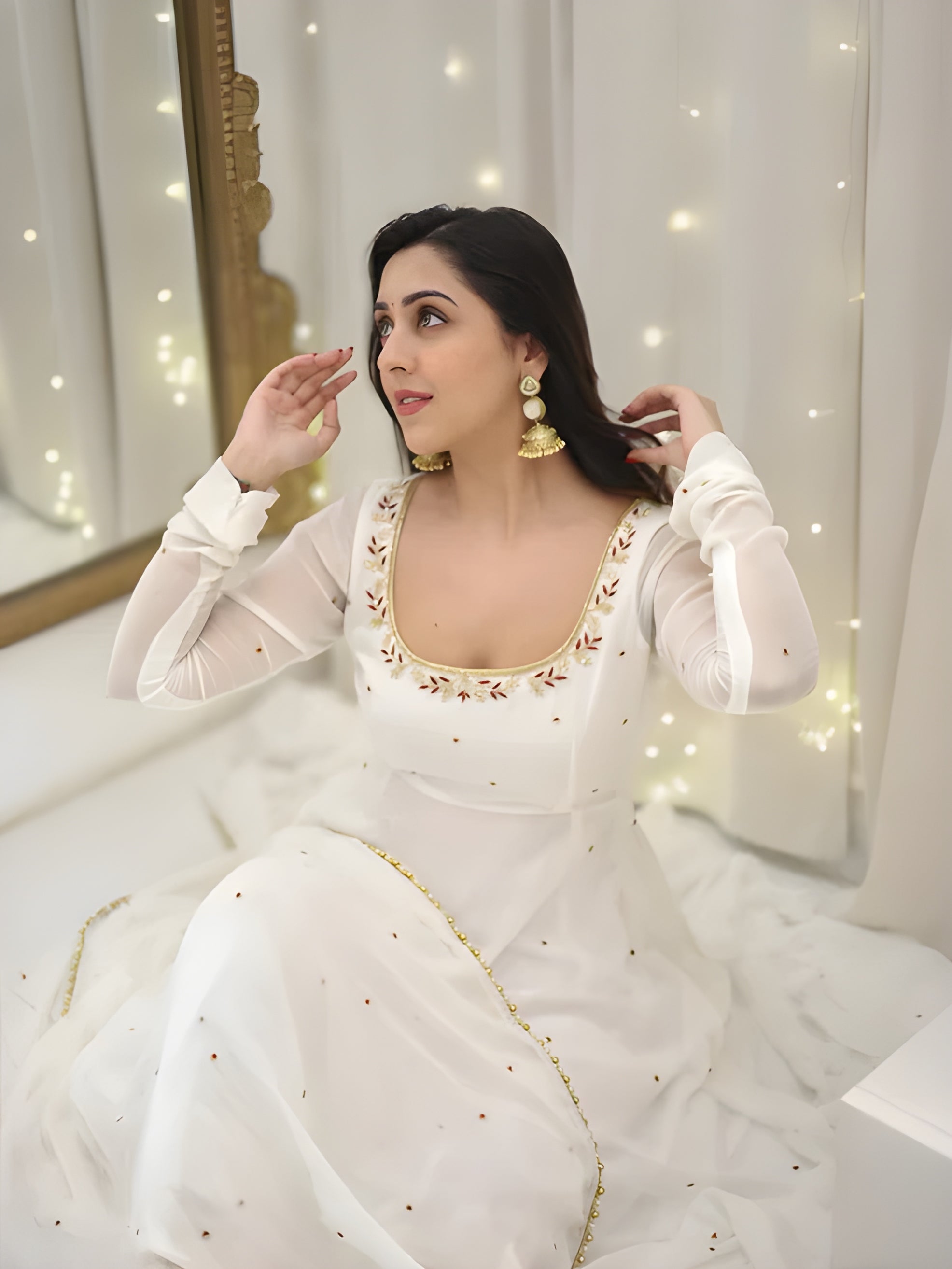 Woman in a white traditional outfit with gold details sitting in front of a mirror.